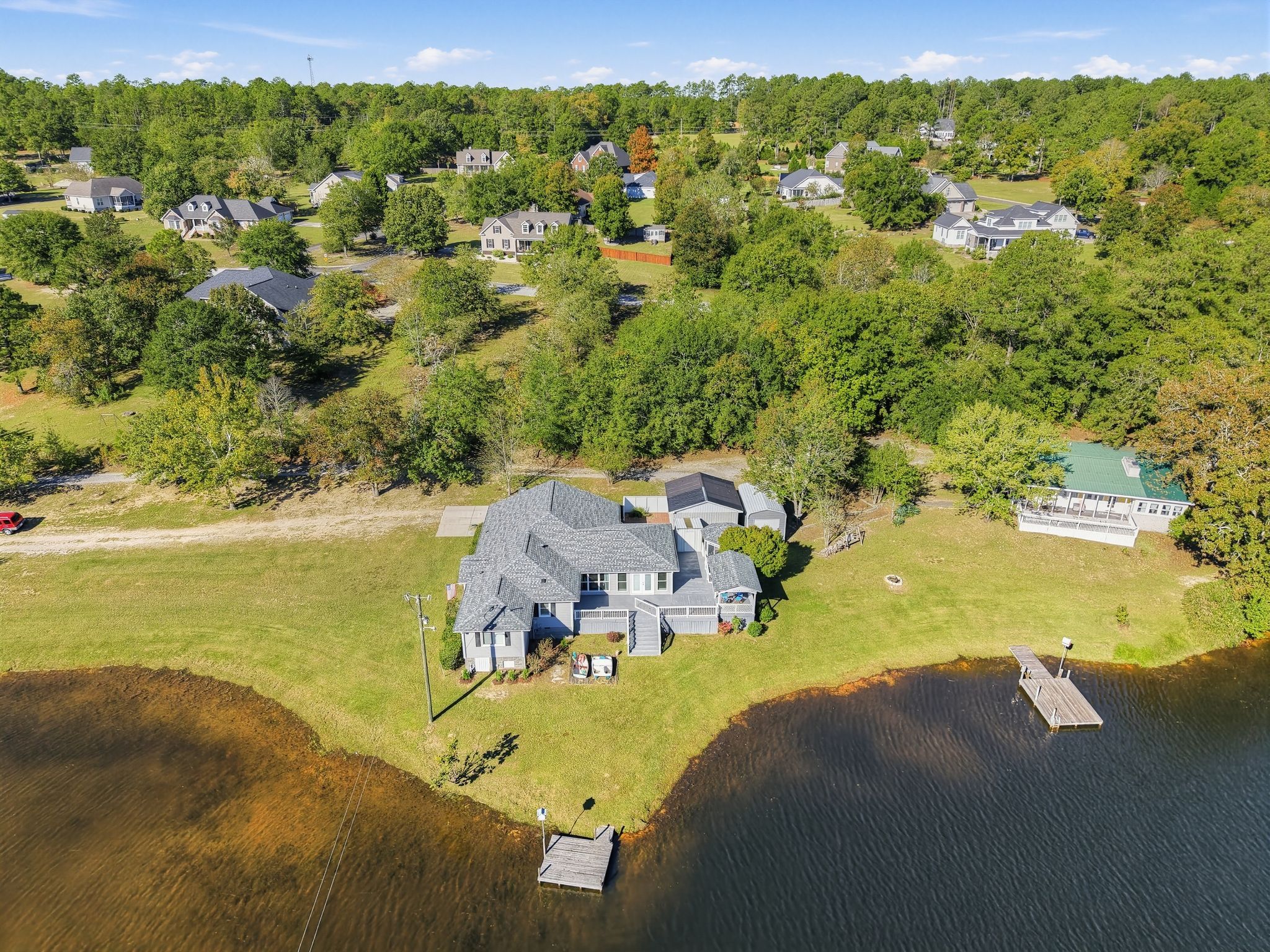 Une grande maison avec un quai et un petit bateau, entourée d’un lac et d’une forêt dense.