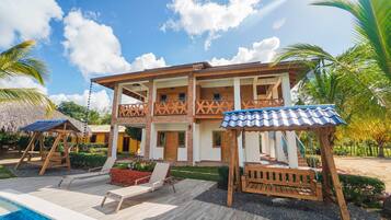 A two-story building with a pool, wooden deck, and a covered seating area.