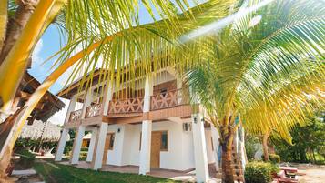 A two-story building with a balcony, surrounded by palm trees and a well-maintained lawn.