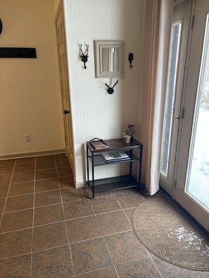 A hallway with a tiled floor, a door with a glass panel, a small table with a tray, and wall-mounted decorations.