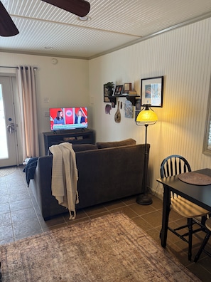 A living room with a sofa, a television displaying a news program, a lamp, and a dining table with a chair.