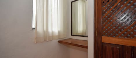 Una habitación con ventana, espejo y puerta de madera con diseño de celosía.