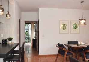 Un coin repas avec une table et des chaises en bois, une cuisine dotée d’un plan de travail noir et d’un grille-pain, et un couloir menant à une porte.