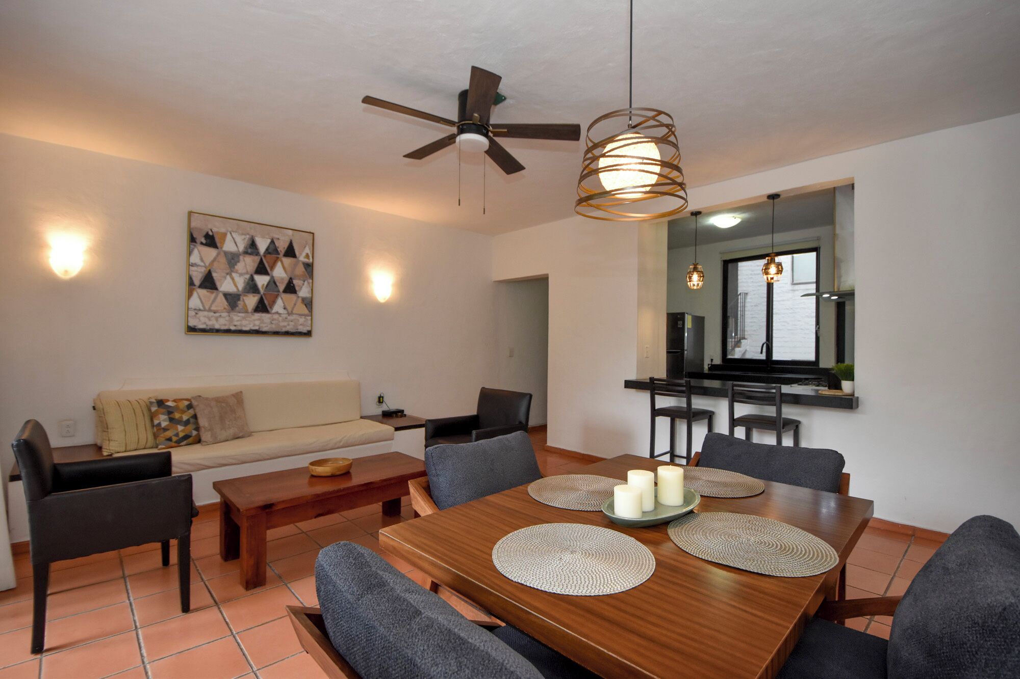 A modern living room with a dining area, a ceiling fan, and a kitchen visible through an open doorway.