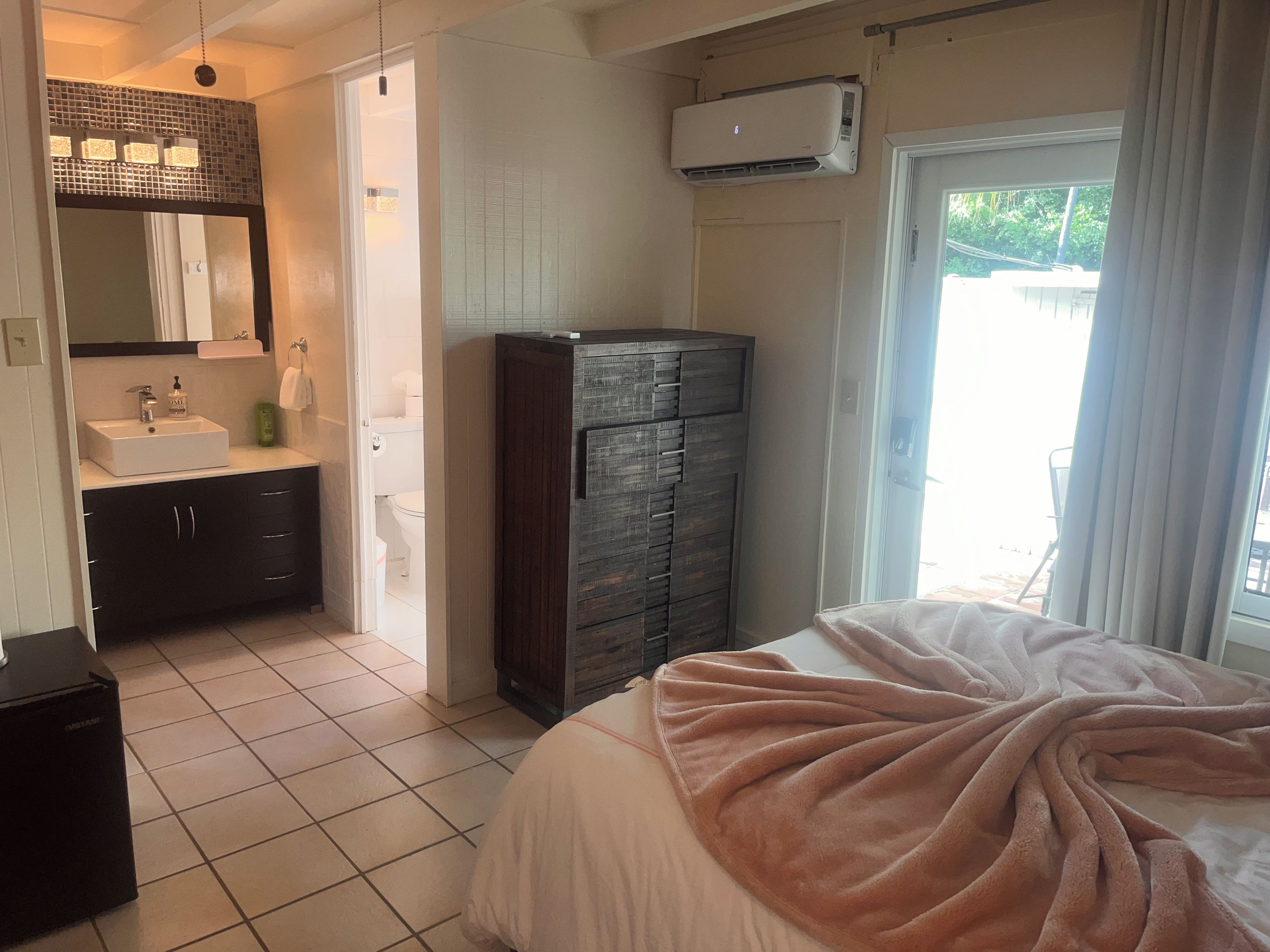 Une chambre à coucher comprenant un lit, une commode, une salle de bain avec un lavabo et un appareil de climatisation.