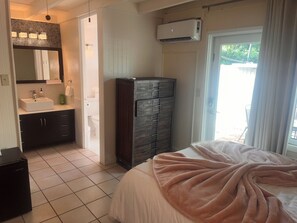 A bedroom with a bed, a dresser, a bathroom with a sink, and an air conditioning unit. - Relaxing 1-bedroom resort in Pineapple Village (Charlotte Amalie)