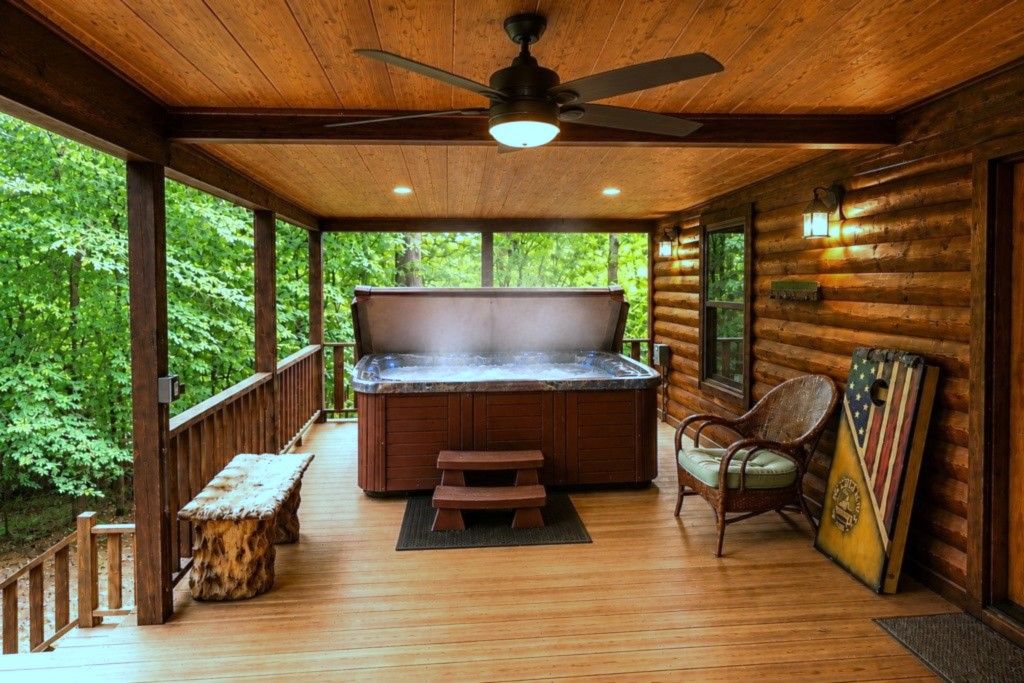Un patio in legno con una vasca idromassaggio, una panca di legno e una sedia.