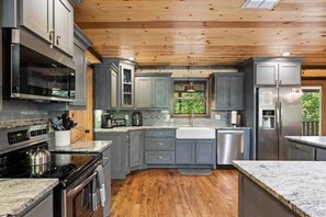 A modern kitchen with grey cabinetry, stainless steel appliances, and a wooden ceiling. - Sweet Sage Lodge -New Pool December 2026! (Broken Bow)