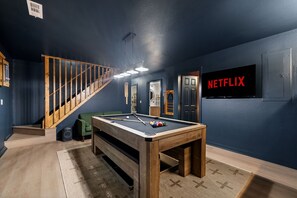 Et værelse med billardbord, trappe og en dør med teksten 'NETFLIX'.