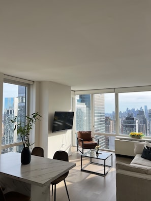 A modern living room with a large window, a flat-screen TV, a dining table, a sofa, and a chair.