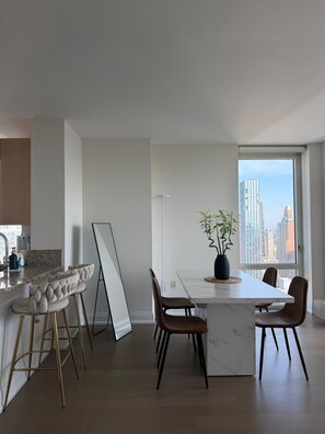 Una cocina moderna con encimera de mármol, una zona de comedor con mesa y sillas blancas, y un ventanal con vistas a la ciudad.