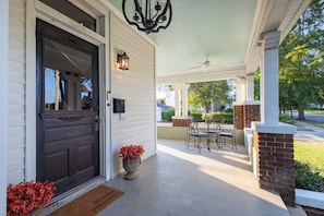 A covered porch with a dark wooden door, a mailbox, and a small table with chairs.