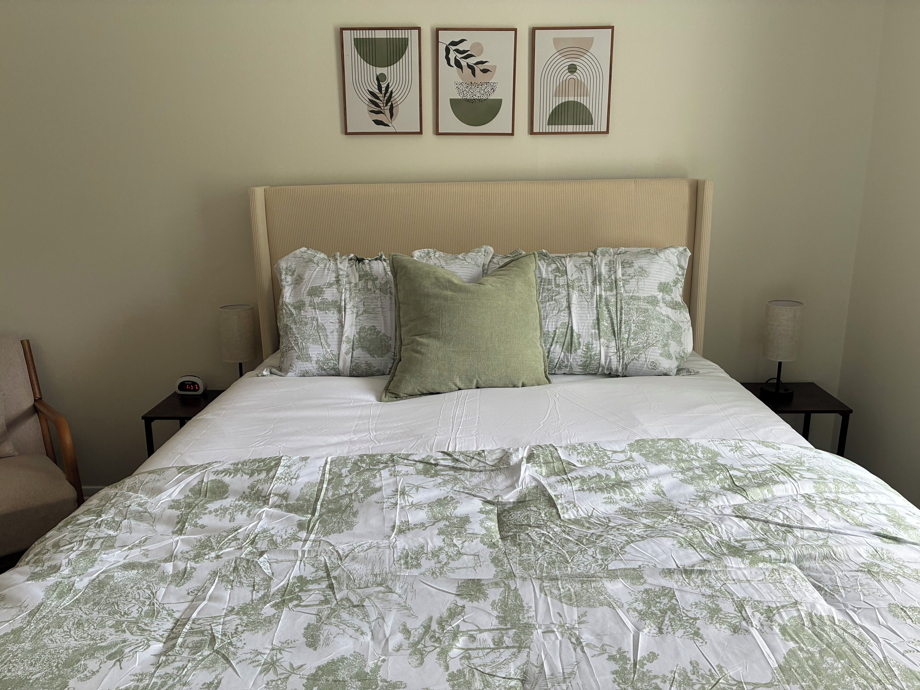 Una cama con colcha estampada de flores, cabecero con diseño fruncido y tres obras de arte enmarcadas sobre la cama.