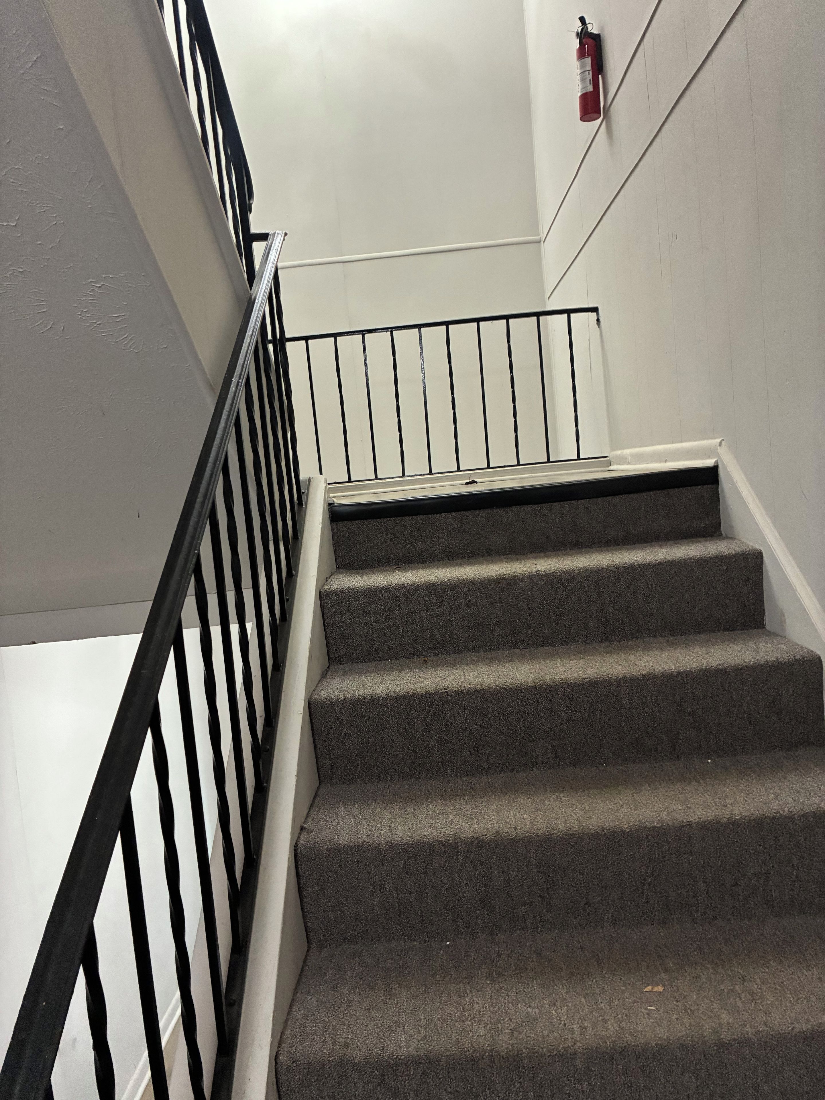A staircase with a black metal railing and a fire extinguisher mounted on the wall.