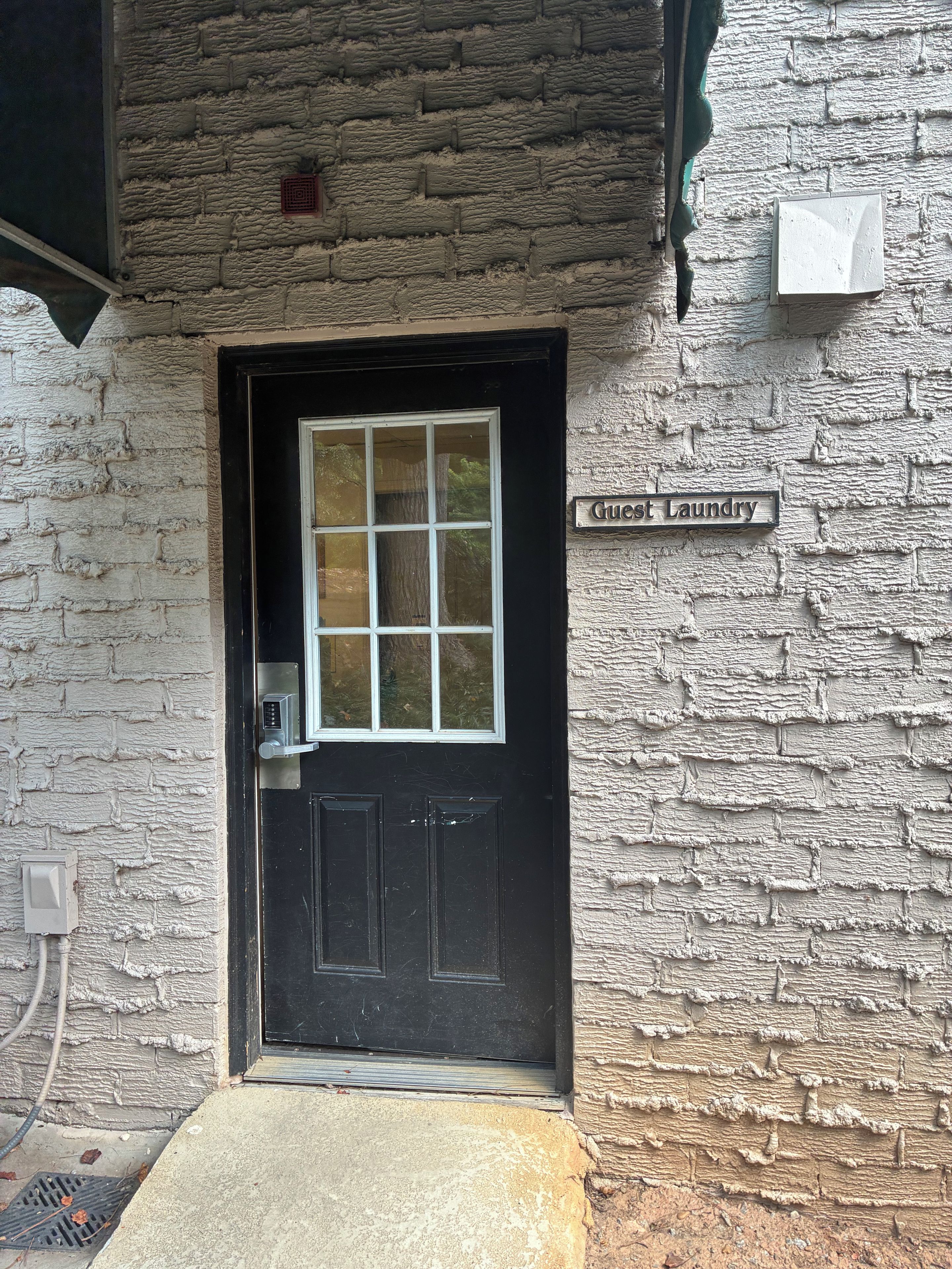 A black door with a window, a 'Guest Laundry' sign, and a textured wall.