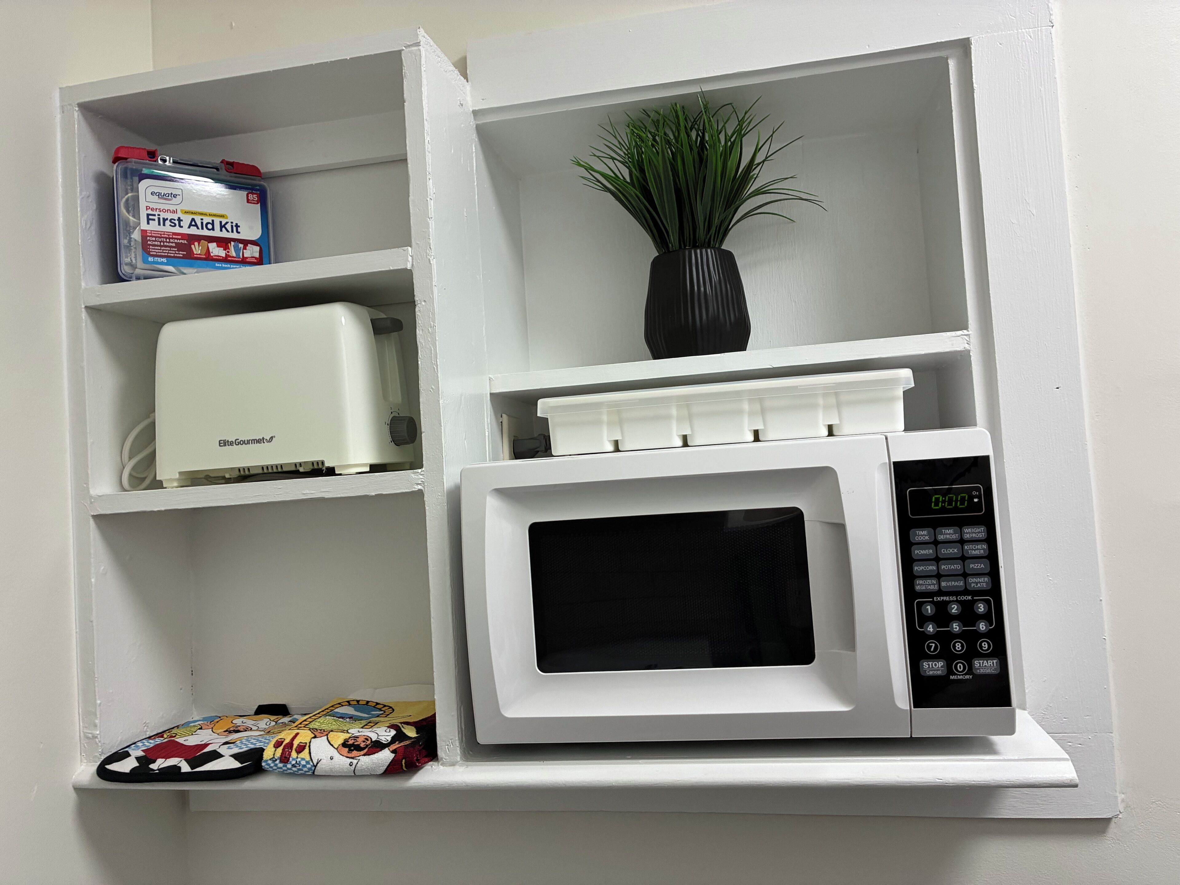 A white microwave oven with a digital display and control panel, placed on a white shelf.