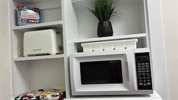 A white microwave oven with a digital display and control panel, placed on a white shelf.