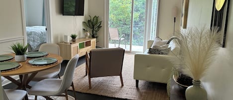 Un salon moderne comprenant un coin repas, un téléviseur à écran plat fixé au mur et une vue sur la verdure grâce aux portes-fenêtres coulissantes.