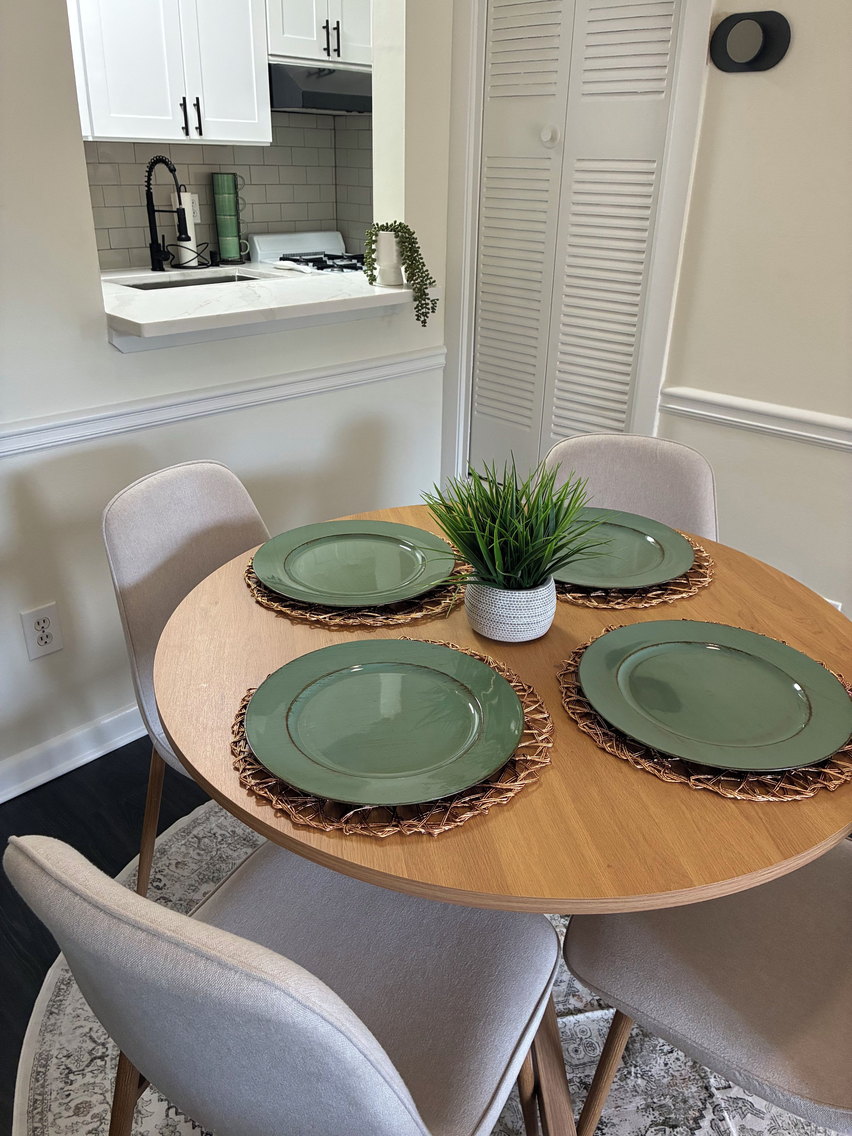 A dining table with four green plates and a small potted plant.