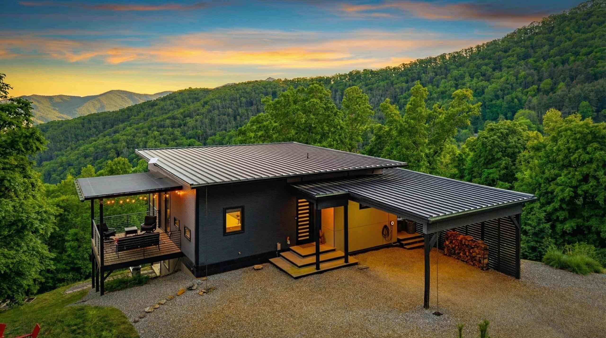 Une maison moderne dotée d’une grande terrasse et d’un espace extérieur couvert, le tout entouré de collines boisées.