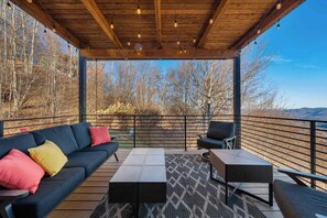 Um deck externo com teto de madeira, um sofá, uma cadeira e uma mesa.