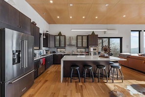 Une cuisine moderne avec des meubles de couleur sombre, des appareils en acier inoxydable et un îlot central doté de tabourets de bar.