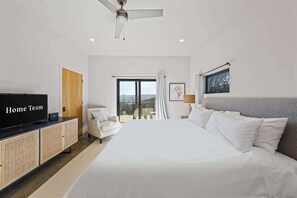 Quarto de hotel com cama, televisão, ventoinha no teto, janela com cortinas e vista para o exterior.