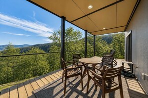 Eine Terrasse im Freien mit Tisch und Stühlen mit Blick auf eine bewaldete Landschaft.