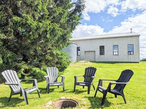 A grassy outdoor area with four Adirondack chairs and a metal fire pit.