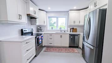 Una cocina moderna con armarios blancos, electrodomésticos de acero inoxidable y un ventanal que aporta luz natural.