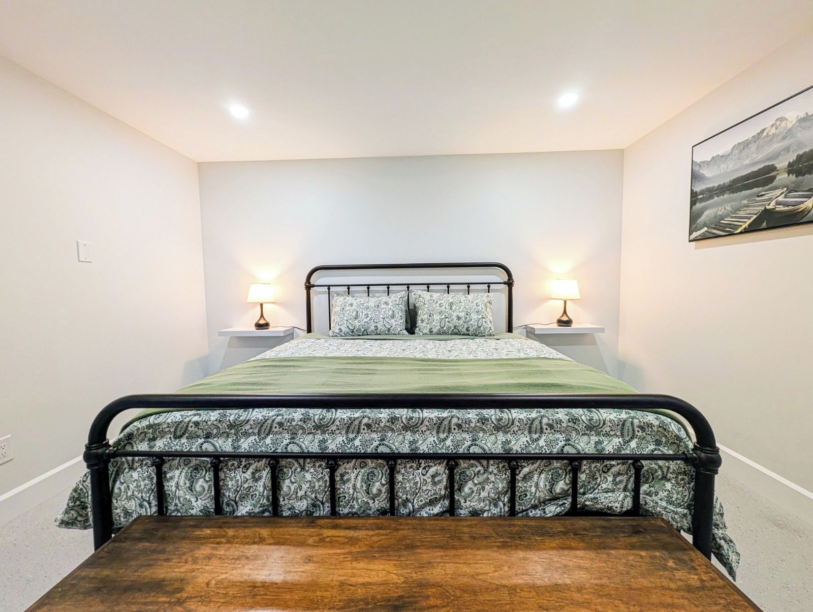 A bedroom with a bed, bedside lamps, a wooden bench, and a painting on the wall.