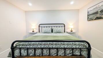 A bedroom with a bed, bedside lamps, a wooden bench, and a painting on the wall.