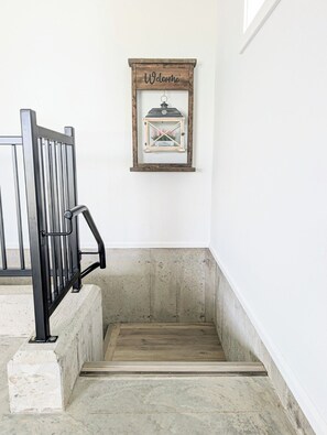 A staircase with a metal railing, a wooden floor, and a wall-mounted welcome sign with a lantern illustration.