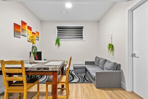 A compact living space with a dining area, a sofa, and a window with blinds. - 2BHK Close to Downtown/Whyte Ave/UOFA 10633 (Edmonton)