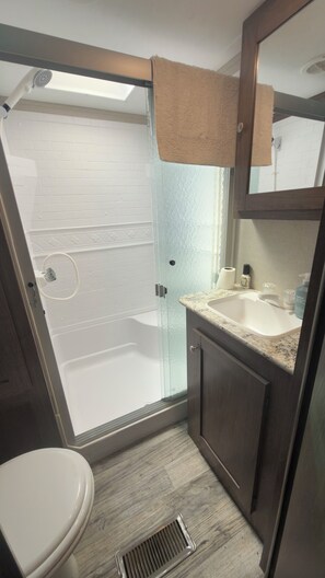 Une salle de bain avec une douche à parois de verre, des toilettes blanches, un lavabo avec un plan de travail en marbre et un meuble en bois.