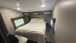 Une pièce étroite et faiblement éclairée, avec un lit, un petit bureau et une chaise.
