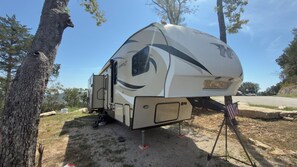 A recreational vehicle parked outdoors with a side door, a small attached structure, and an American flag. - Lakeview RV with large deck, 1 mile to marina (Shell Knob)