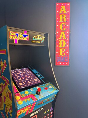 Une borne d’arcade ancienne, dotée d’un écran coloré et d’une enseigne verticale sur laquelle on peut lire « JEUX D’ARCADE ».