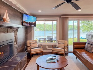 A living room with a fireplace, a television mounted on the wall, and a view of a lake through large windows. - Lakefront - Kids' Hangout - Fire Pit - Kayaks (Barnstead)