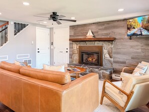 A living room with a stone fireplace, leather sofa, and a television mounted on the wall. - Lakefront - Kids' Hangout - Fire Pit - Kayaks (Barnstead)