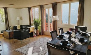 A dining area with a table set for four, a sofa, and a potted plant. - STUNNING WENGEN CHALET WITH HOT TUB & ALPINE VIEWS (Lauterbrunnen)