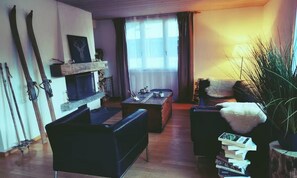 A living room with a fireplace, a sofa, a coffee table, and skis leaning against the wall. - STUNNING WENGEN CHALET WITH HOT TUB & ALPINE VIEWS (Lauterbrunnen)