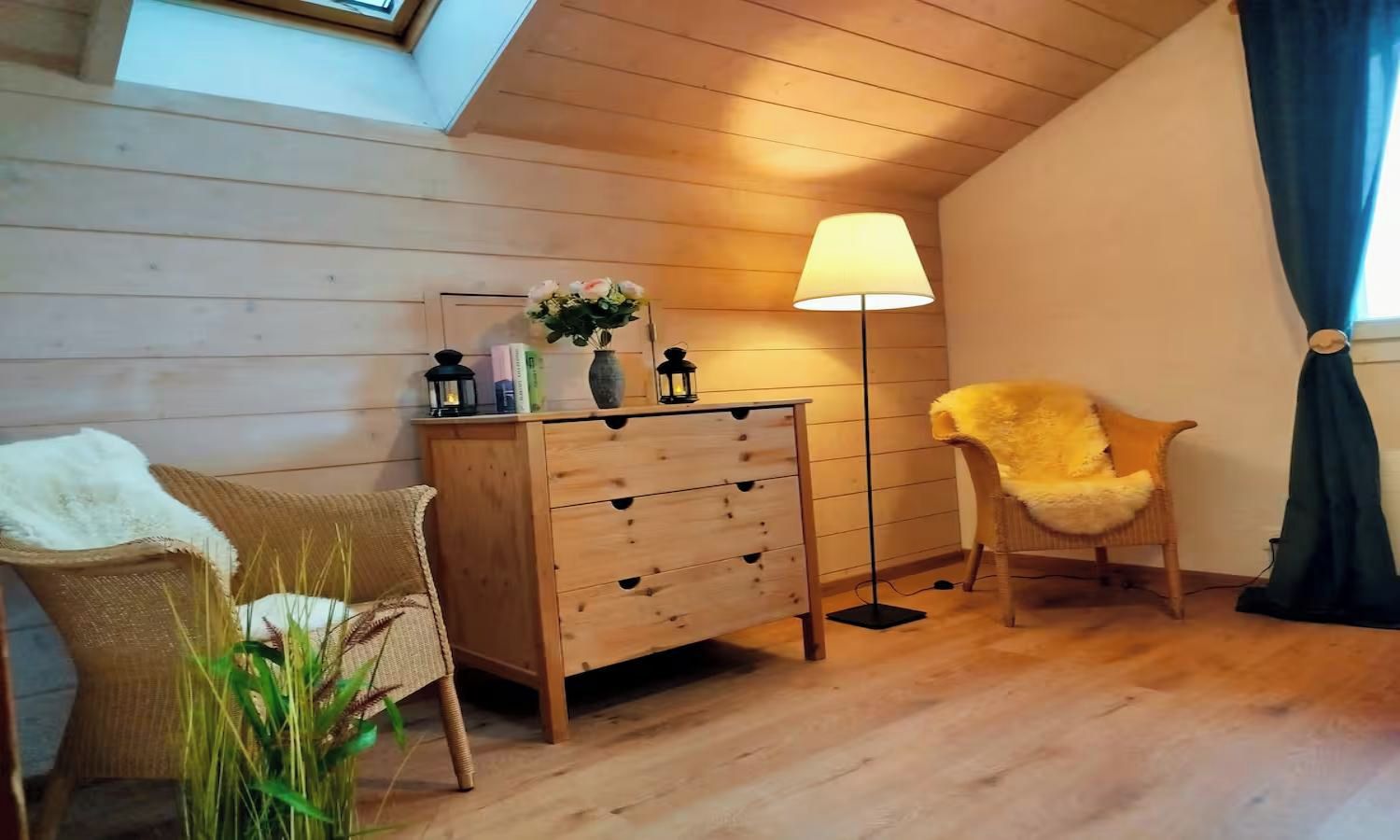 A cozy room with a wooden dresser, two chairs, a floor lamp, and a plant.