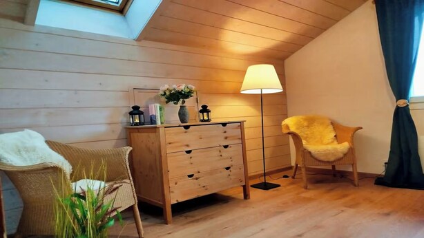 Une pièce chaleureuse avec une commode en bois, deux chaises, une lampe sur pied et une plante.
