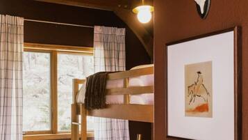 Une chambre avec un lit superposé, une fenêtre, un tableau encadré et une tête d’animal fixée au mur.