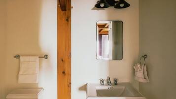 A bathroom with a white sink, two wall-mounted lights, a mirror, and a towel rack.