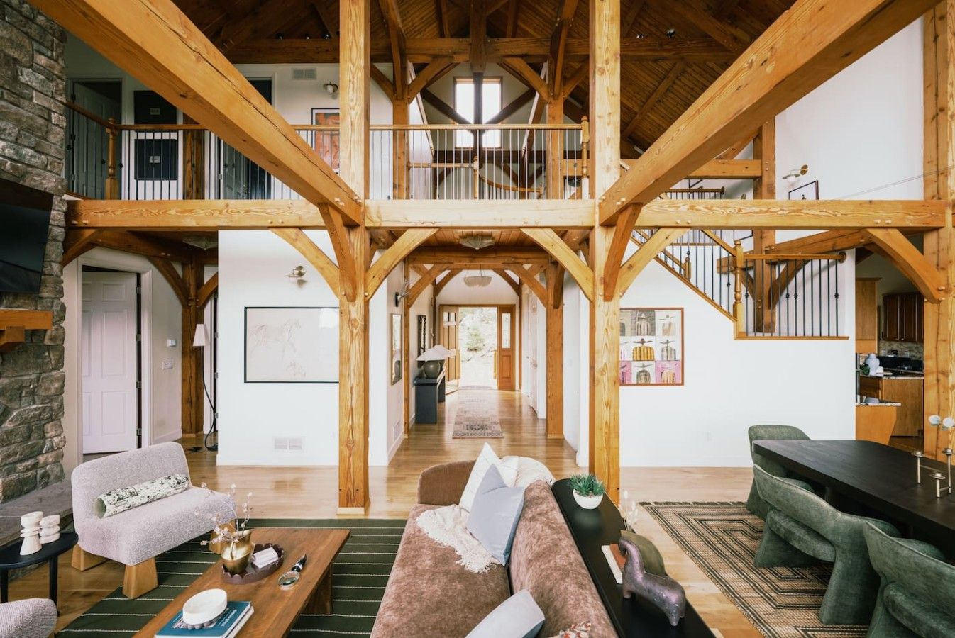 A spacious loft with exposed wooden beams, a central staircase, and a view of the kitchen.
