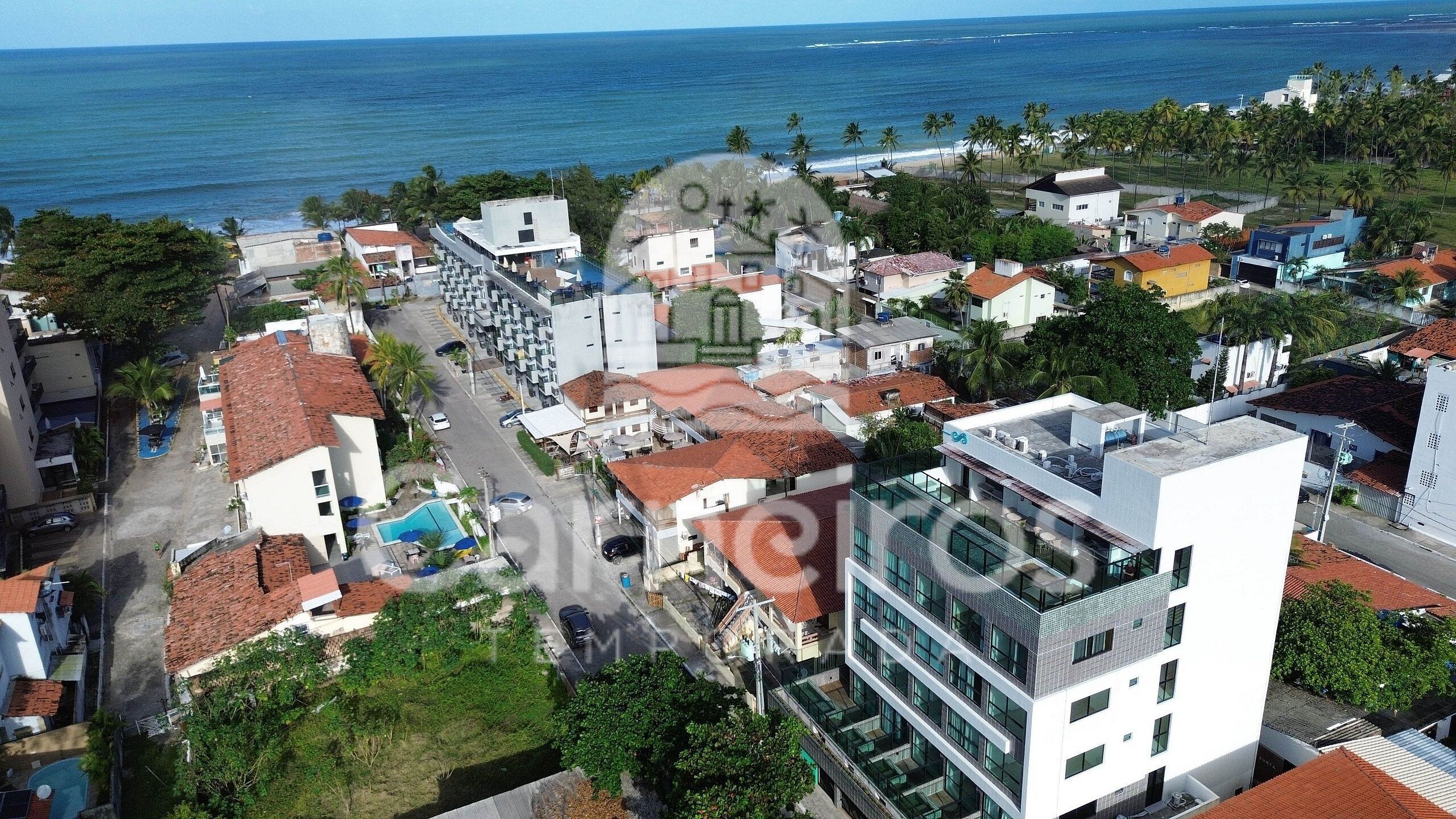 Une vue aérienne d’une ville côtière, avec ses bâtiments, une piscine et une vue sur l’océan.