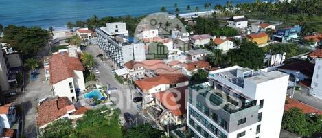 An aerial view of a coastal town with buildings, a swimming pool, and a view of the ocean.