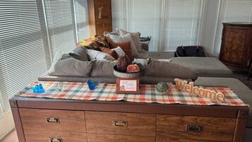 A cozy living room with a sofa, decorative pillows, a welcome sign, and a plaid table runner.